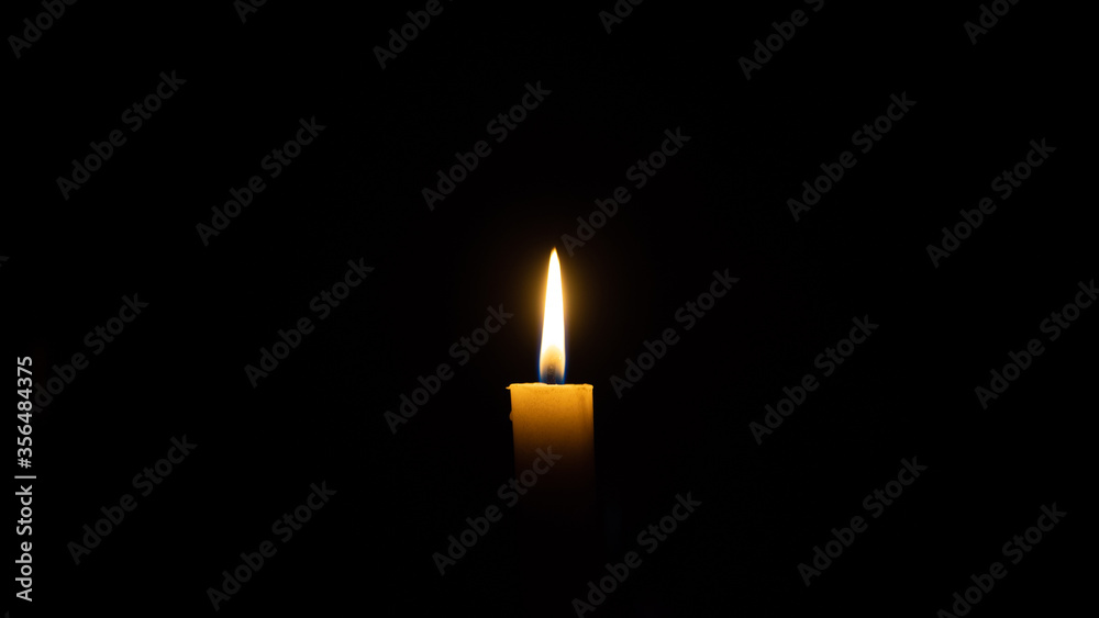 A candle burns in the darkness, copy space. A lit white candle on a black background. Symbol of eternal memory, mourning, minutes of silence, memorial day. The concept of loss and to the memory A candle burns in the darkness, copy space. A lit white candle on a black background. Symbol of eternal memory, mourning, minutes of silence, memorial day. The concept of loss and to the memory