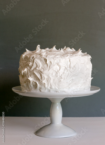 Frosted white cake on stand with gray background