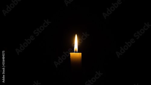 A candle burns in the darkness, copy space. A lit white candle on a black background. Symbol of eternal memory, mourning, minutes of silence, memorial day. The concept of loss and to the memory
