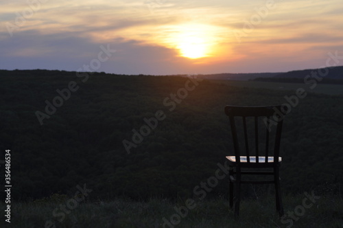 An old antique chair stands on the grass. At sunset. Summer. The concept of meditation and loneliness.