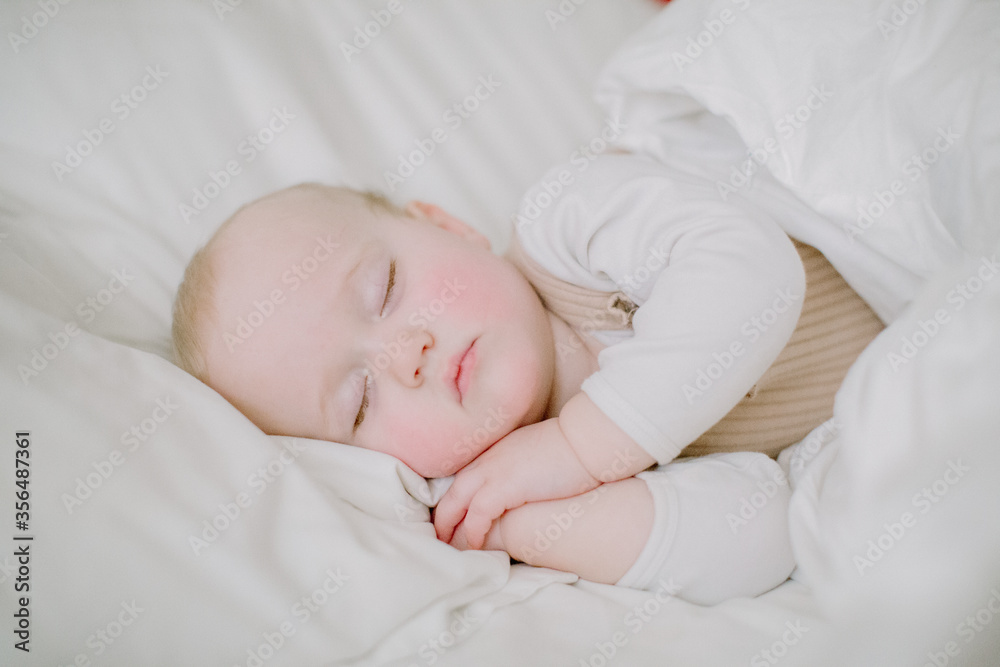 Baby girl sleeping peacefully in white bed facing camera with hands fo Baby girl sleeping peacefully in white bed facing camera with hands fo