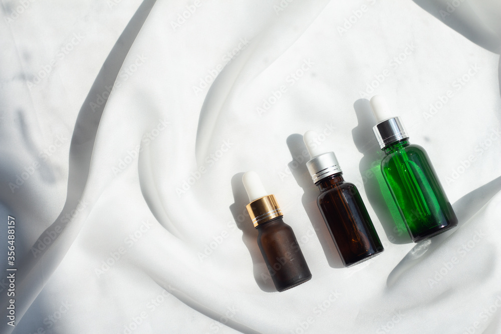 glass bottle of Natural facial essential oil or serum packaging on white fabric background. Beauty product branding mock-up. Cosmetic skincare concept. Minimal and luxury. glass bottle of Natural facial essential oil or serum packaging on white fabric background. Beauty product branding mock-up. Cosmetic skincare concept. Minimal and luxury.