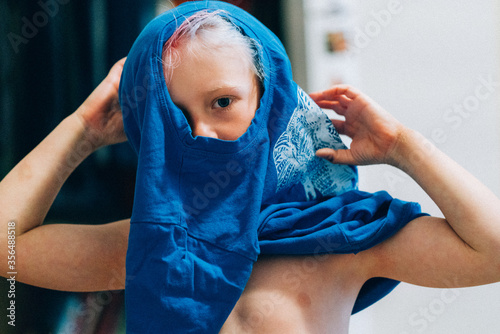 Child putting shirt on looking at camera
