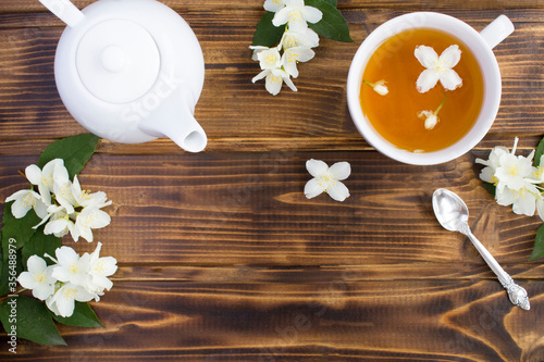 Jasmine green tea in the white cup, teapot and flowers on the brown wooden background. Top view. Copy space.