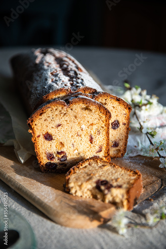 Sliced homemade pound cake with dried berries, vintage glass plates and blooming cherry twigs on linen tablecloth.