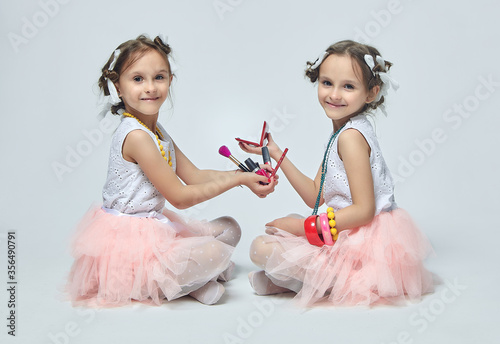 two little girls play with their mother's makeup. they pose and try to be adults.Studio, white background