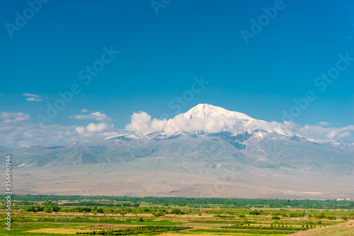 Ararat peak behind the clouds on a background of green field, beautiful landscape of Armenia