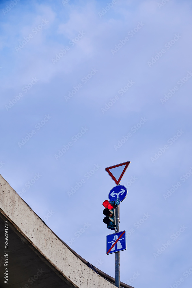 Bottom view of a red traffic light and various traffic signs at an intersection on a bridge in Berlin, Germany.