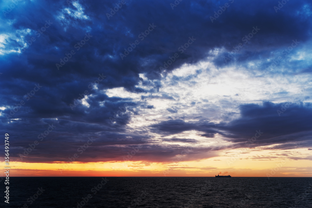 Beautiful scene of dark blue clouds above sea and ship silhouette at horizon during sunset