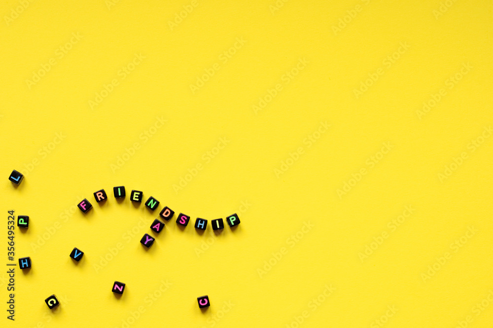Naklejka premium The word friendshipday composed from cubes with multicolored letters on a yellow background. A close-up.