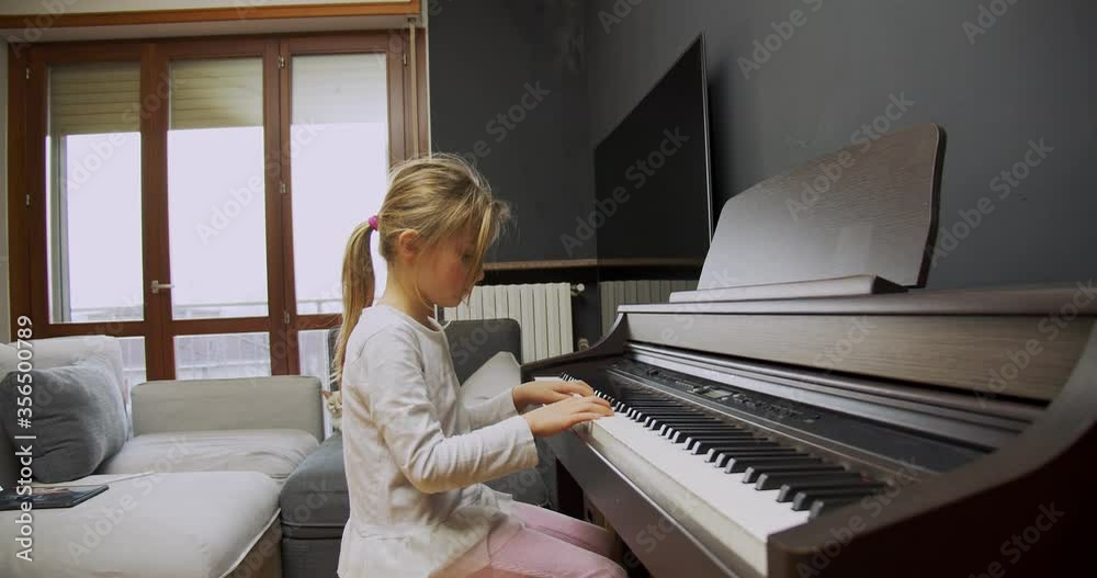 Little girl playing piano at home. Kid play piano in living room. Child learning piano at home. Music lesson, medium shot side view.