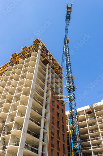 Construction crane at the construction of monolithic apartment building. Building construction site with crane on the blue sky background. The construction of modern multifamily apartment buildings