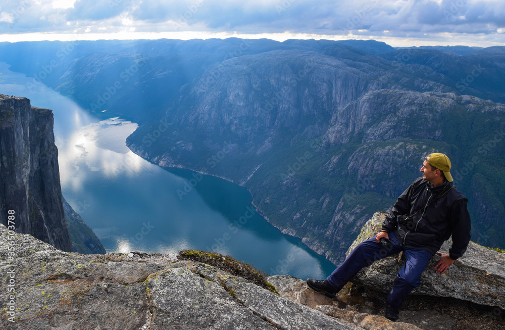Tourist man on the edge above Lysefjorden. Wonderful mountain landscape with clouds reflected in blue water. Norway, Tourist man on the edge above Lysefjorden. Wonderful mountain landscape with clouds reflected in blue water. Norway,