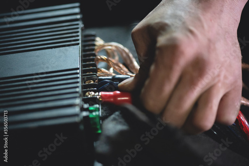 Auto electrician is connecting a wiring to car amplifier close up.