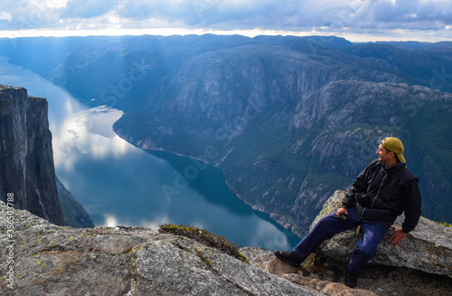 Tourist man on the edge above Lysefjorden. Wonderful mountain landscape with clouds reflected in blue water. Norway,