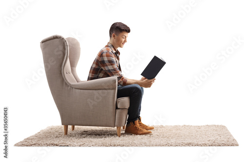 Profile shot of a young man sitting in an armchair and reading a book