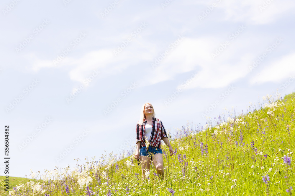 Happy adventurer female stands on the green mountain slope among flowering pink rhododendrons and looking into the distance. Epic travel in the mountains. Wide angle. Happy adventurer female stands on the green mountain slope among flowering pink rhododendrons and looking into the distance. Epic travel in the mountains. Wide angle.