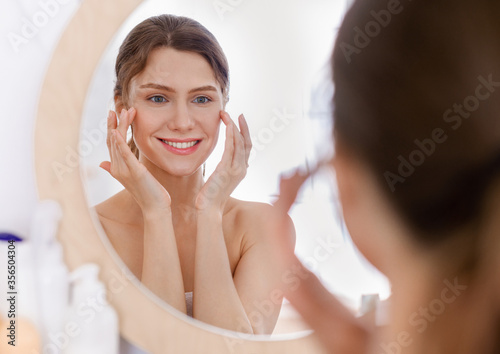 Beautiful woman looking at mirror and applying eye serum