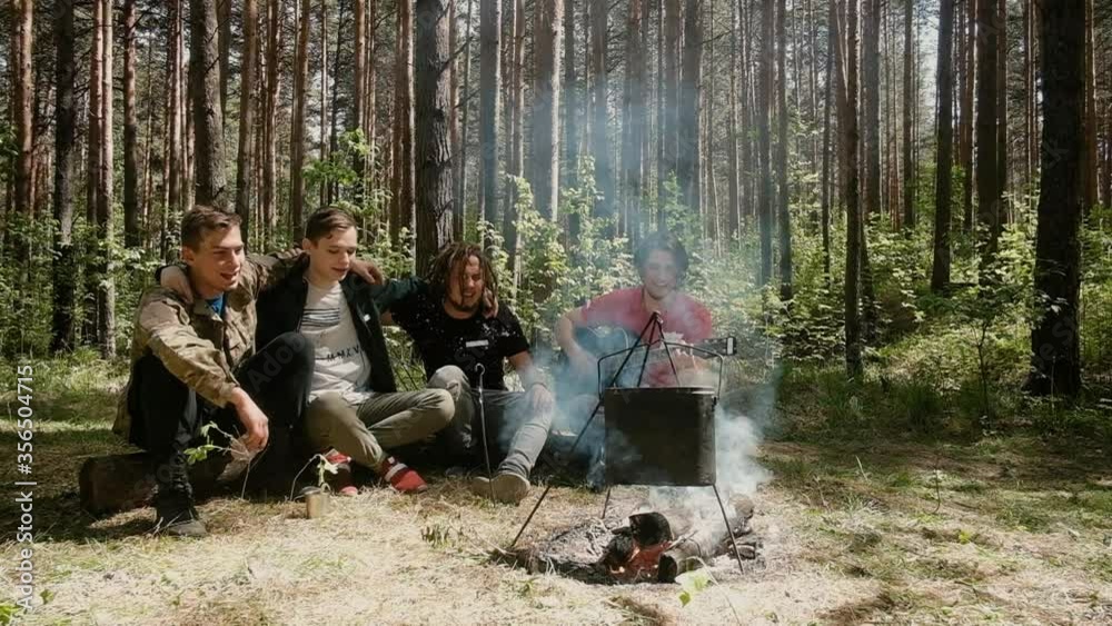 mens are sitting by the fire in the woods. They play the guitar on a hike. They sing songs happily. Fun is fun. Active lifestyle in nature. summer trip. Friendship and leisure concept. mens are sitting by the fire in the woods. They play the guitar on a hike. They sing songs happily. Fun is fun. Active lifestyle in nature. summer trip. Friendship and leisure concept.