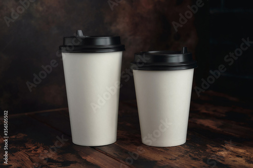 Mock up, white paper cups with a black plastic lid stands on a dark background