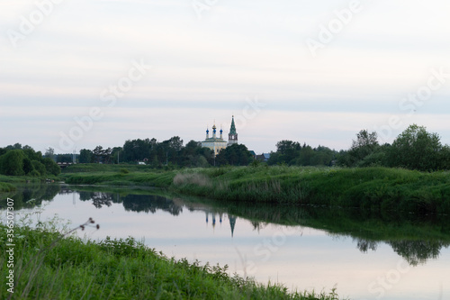 Country landscape in summer evening with river and reflecting church in calm water