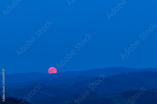 Red moon rising from a mountain area after sunset.