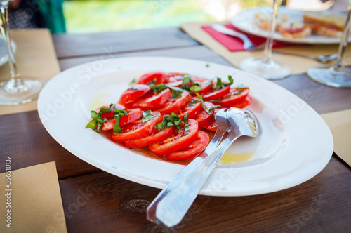 Fresh sliced Italian tomatoes wtih basil and olive oil on a white plate.