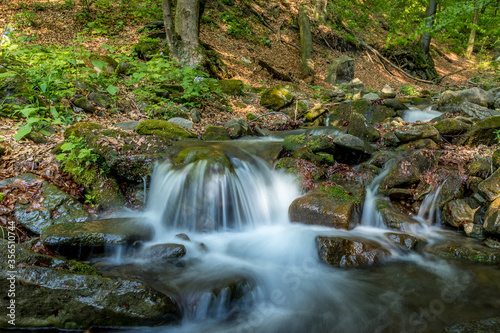A mountain stream flowing through a landscape in a dense forest captured by long exposure time.