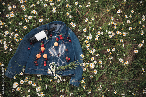 a bottle of wine, two glasses, cherries, strawberries on a denim jacket in a chamomile field