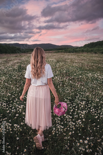 the girl holds a bouquet of pink peonies in her hand