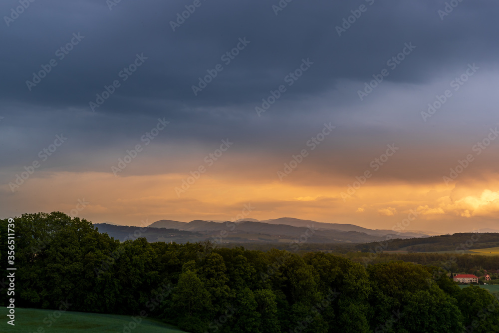 A field of wheat and a view of dark clouds on a hilly landscape before sunset in the distance you can see the rain.