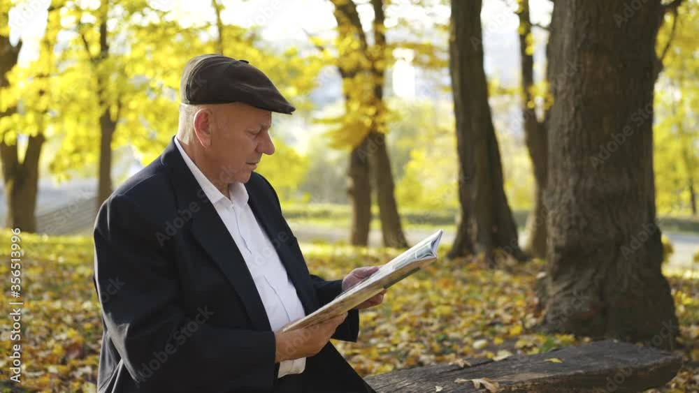Senior man sitting on a park bench and looking at photo album