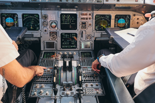 Back view of crop anonymous male captain and pilot sitting in cockpit of modern airplane and checking equipment while preparing for departure