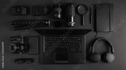 Top view of black modern photography equipment and laptop arranged on dark table.