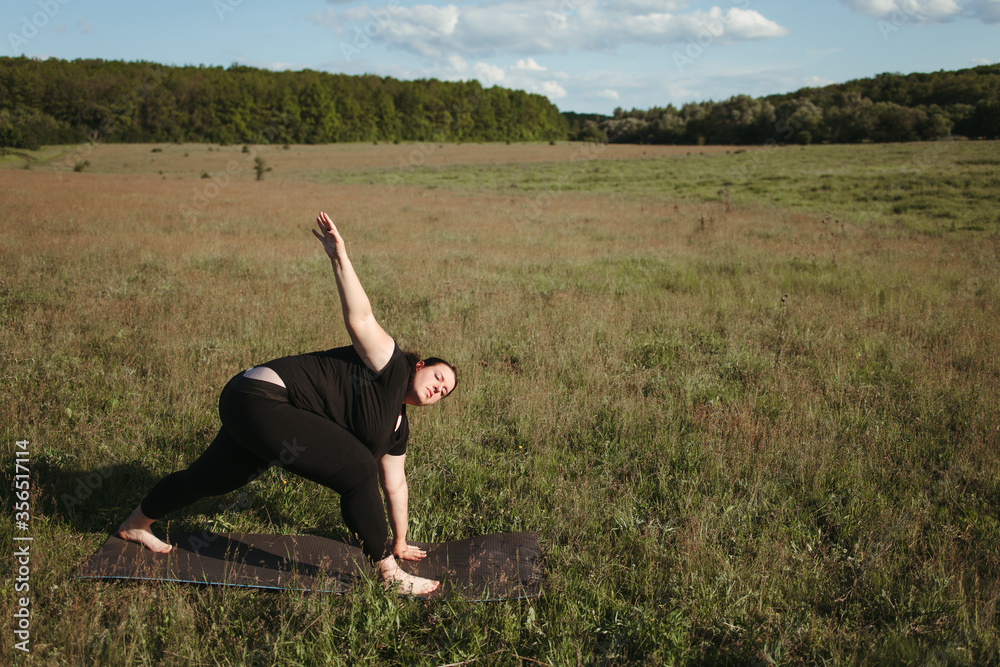 Outdoor yoga. Young overweight woman doing yoga exercise in the meadow. Open air workout, healthy lifestyle, weight loss