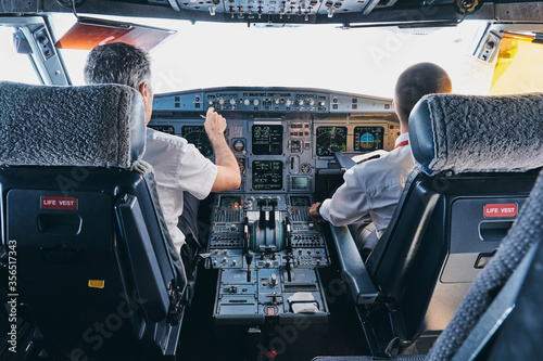 Back view of male pilot and co pilot using instrument panel in cockpit of modern passenger aircraft during flight photo