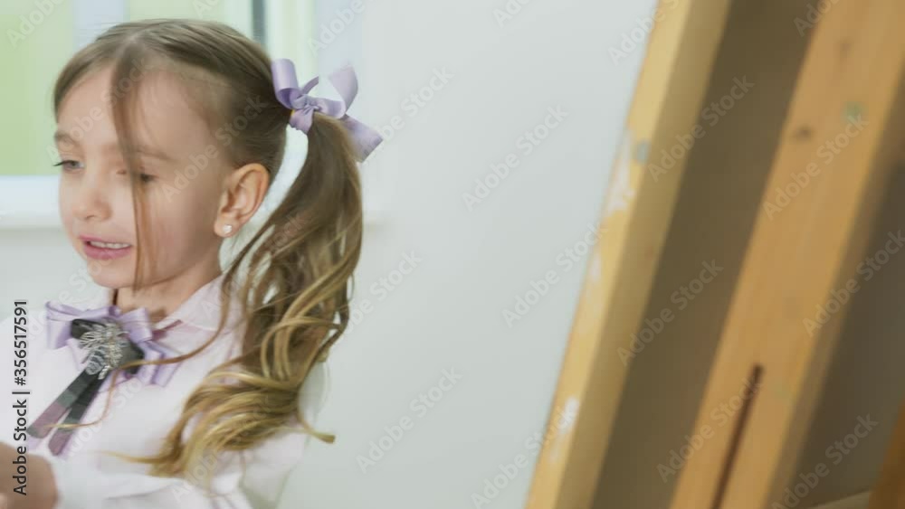 Vidéo Stock little girl paints a picture and looks at the camera. Happy ...