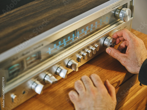High angle of crop hands of unrecognizable male tuning radio placed on wooden shelf in living room