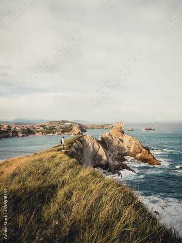 Distant side view of male traveler with backpack and camera standing on rocky seashore and admiring amazing seascape during trip in Spain photo