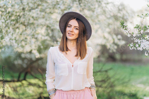 Amazing young woman in hat posing in Blooming tree orchard at spring