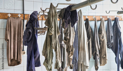 Carelessly scattered dirty miners uniforms hanging on hooks in locker room with white walls tiled in abandoned coal mine photo