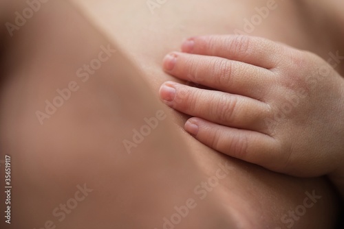 Closeup anonymous nude infant touching soft skin of body while resting at home