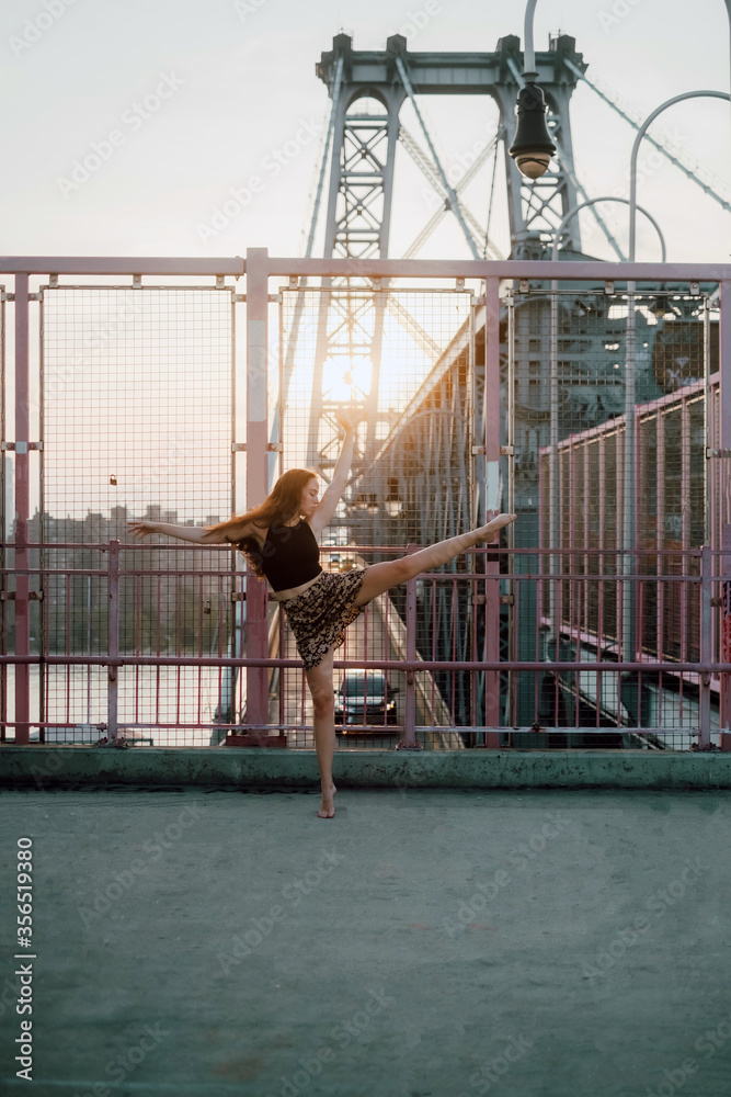 Side view of graceful female dancer in skirt balancing on tiptoe with outstretched arms while practicing choreographic elements on background of cityscape Side view of graceful female dancer in skirt balancing on tiptoe with outstretched arms while practicing choreographic elements on background of cityscape