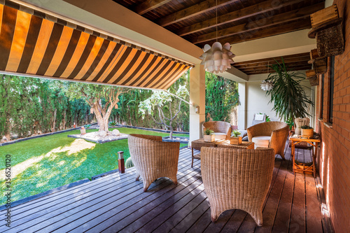 Wooden table with chairs placed on spacious garden terrace of modern country house surrounded with green plants photo