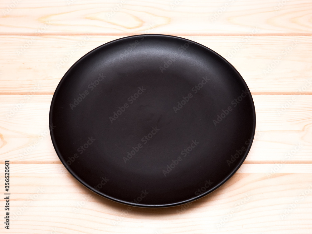 Top view of black empty plate based on the wooden table. Top view of black empty plate based on the wooden table.