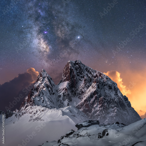 Amazing view of white snowy mountain range under incredible night starry sky with breaking rays of rising sun from behind mountains in winter evening