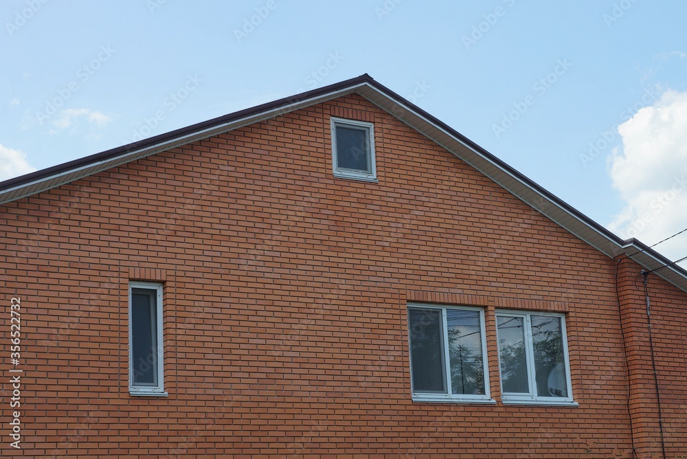 large brown brick loft of a private house with white windows against a blue sky