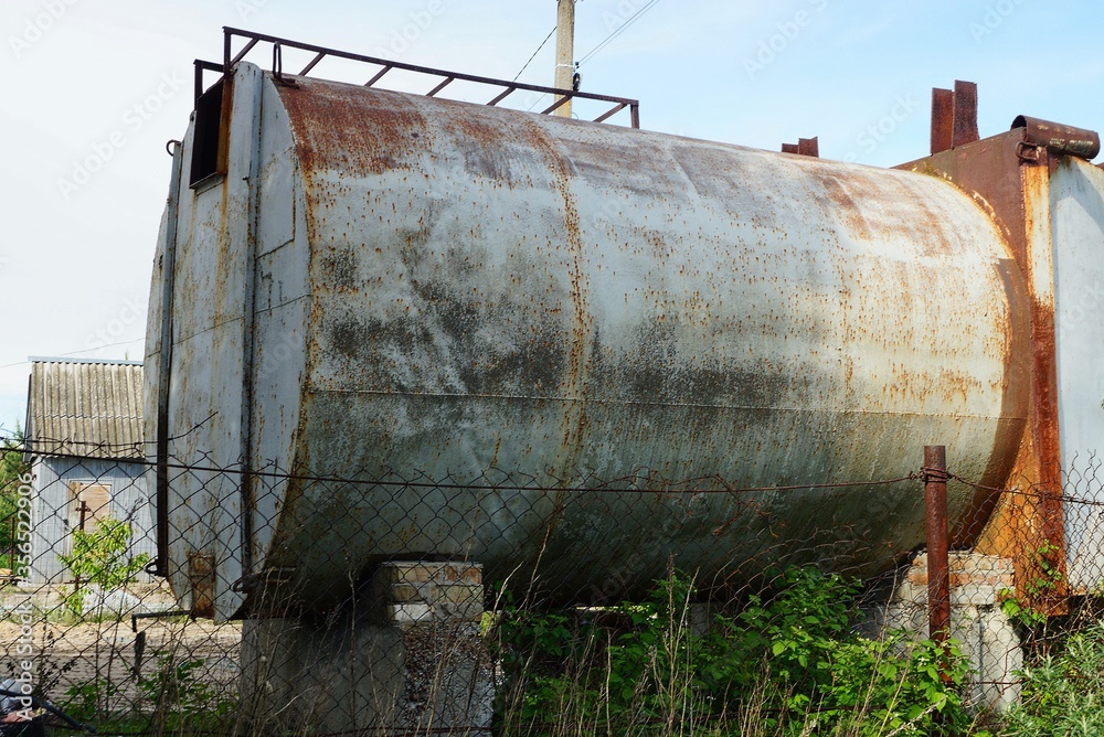 one old iron gray tank in brown rust behind a metal fence on a street one old iron gray tank in brown rust behind a metal fence on a street