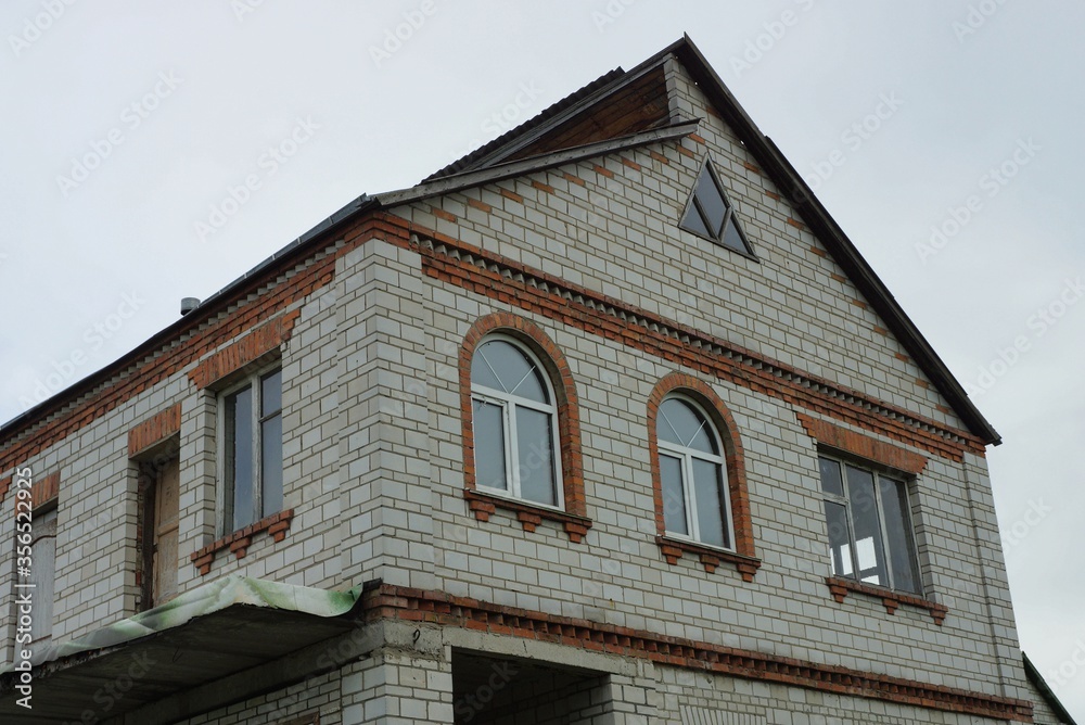 facade of a private house of white bricks with one large windows against a gray sky
