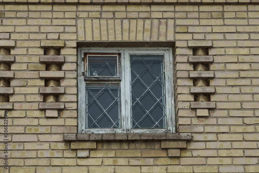 one white old wooden window with iron bars on the brown brick wall of the building
